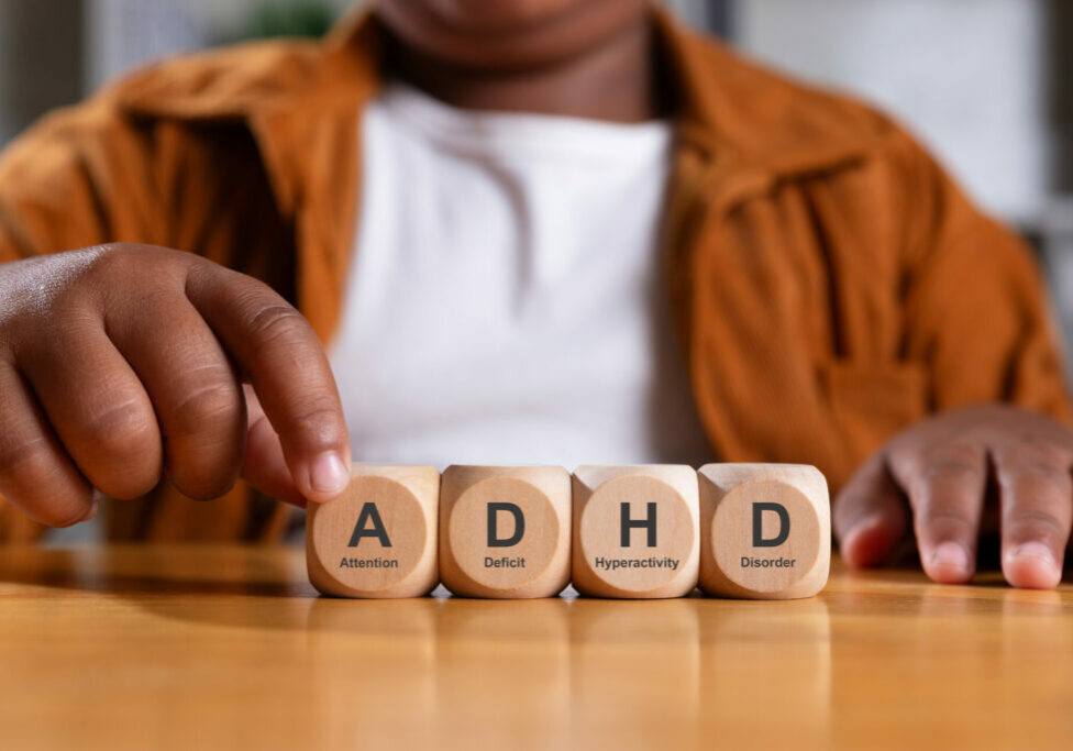 Hand of black boy puts wooden cube with ADHD.